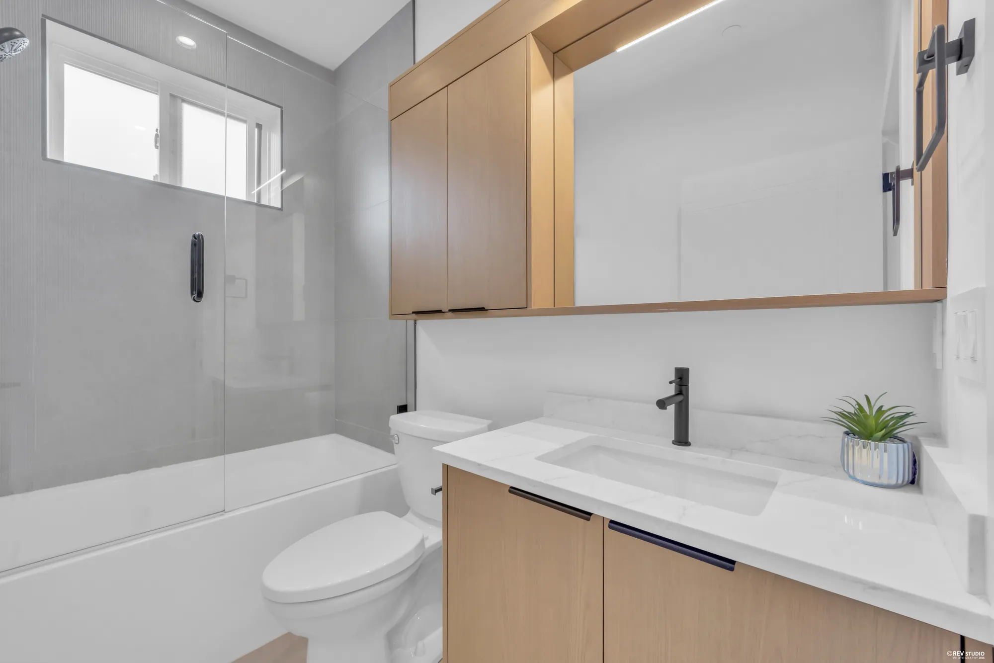 Bathroom with a tub under a window, stone counter and black tapware