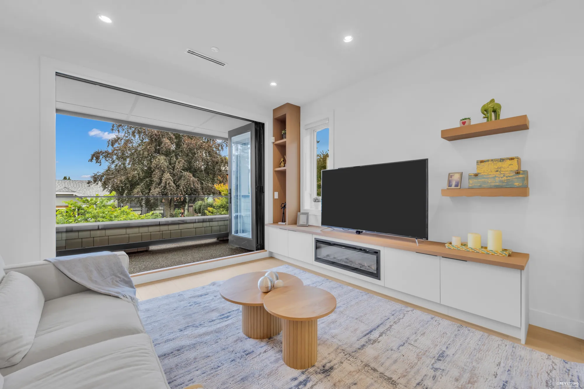 Living room with a pale sofa, round timber coffee table and a linear fireplace under a wall of glass