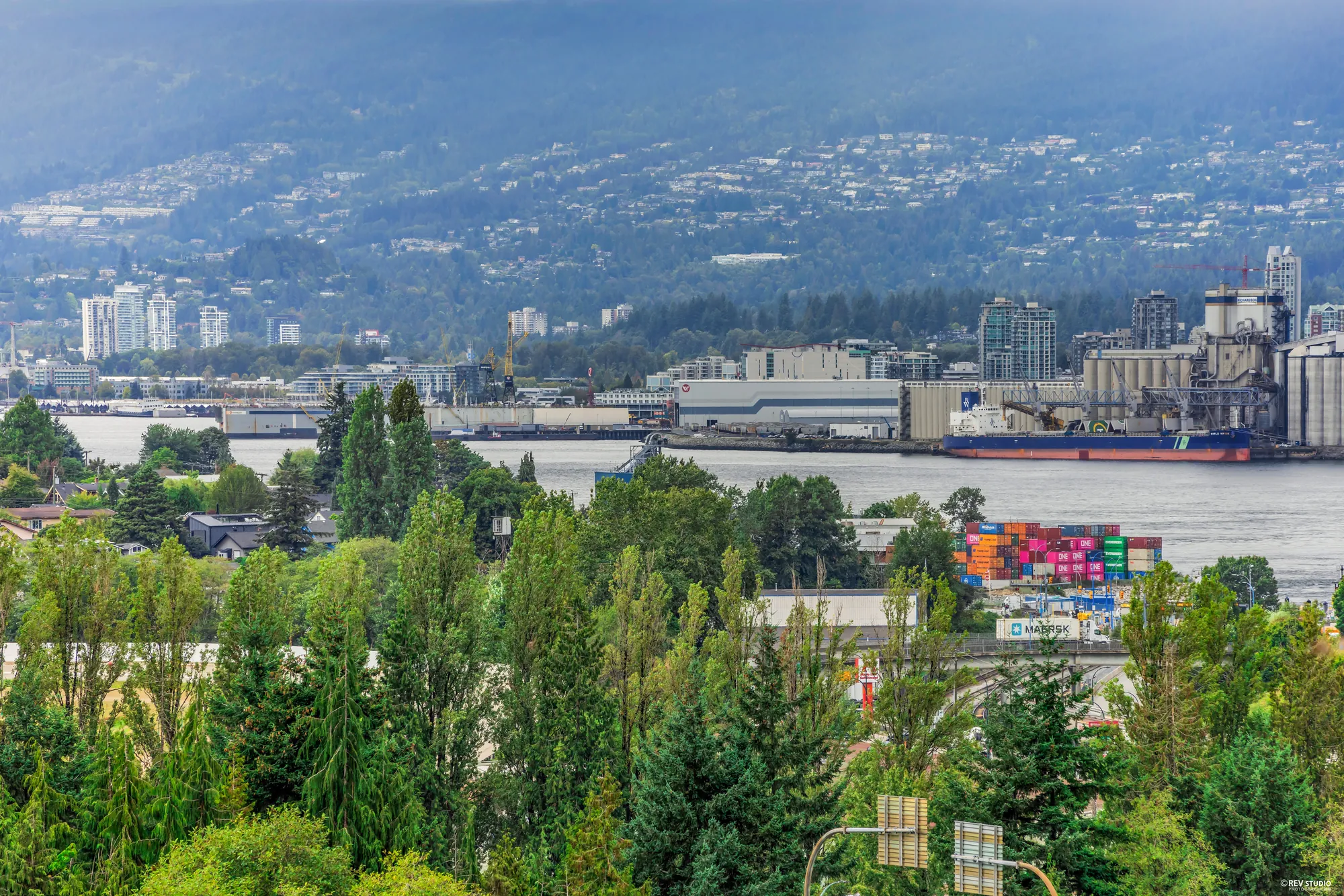 View north over trees and rooftops to Burrard Inlet, the port and the North Shore mountains